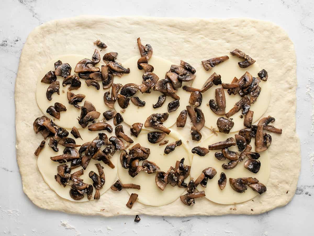 Provolone and mushrooms on pizza dough.
