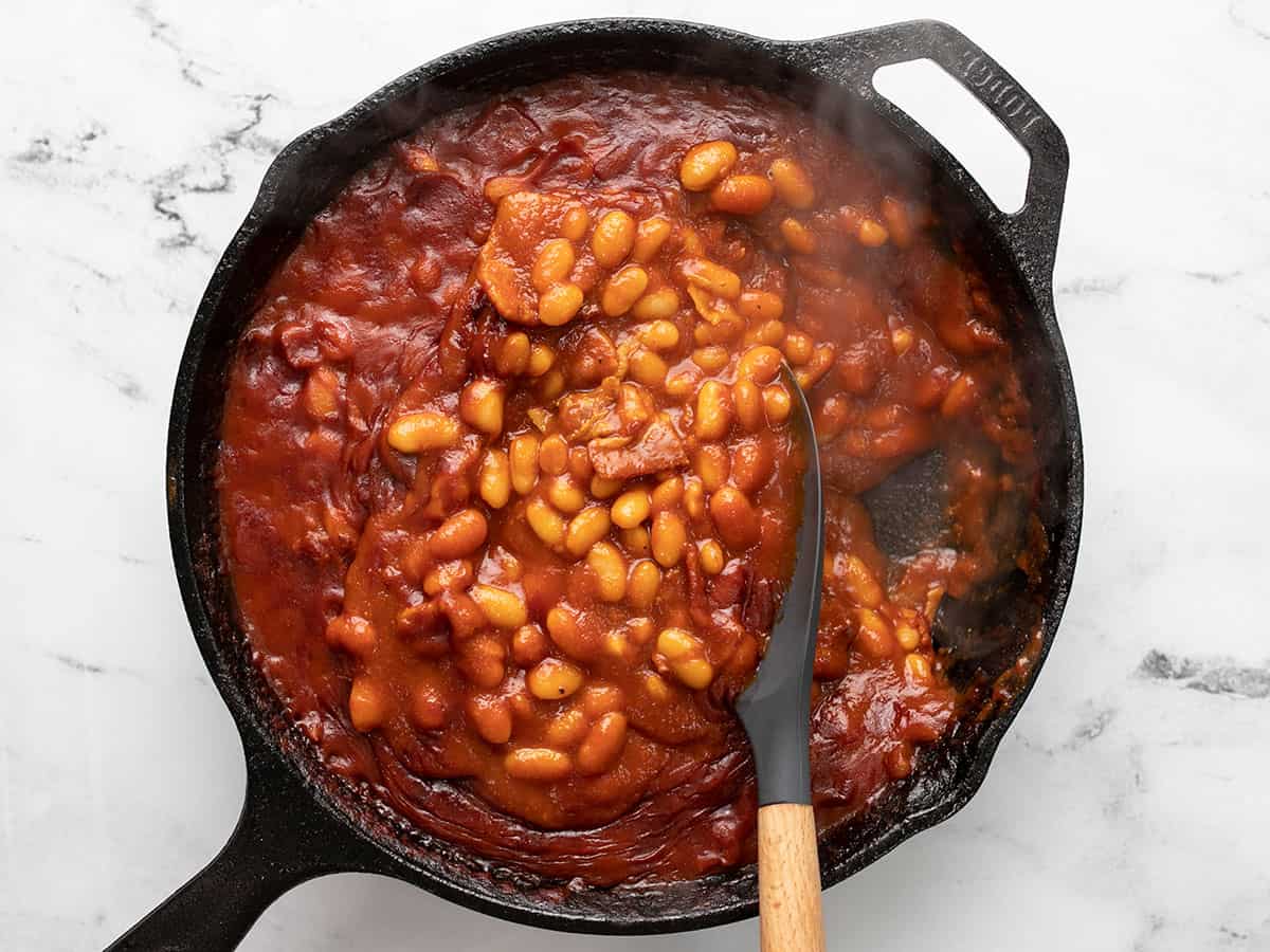 Baked beans after baking, a spoon stirring them slightly.
