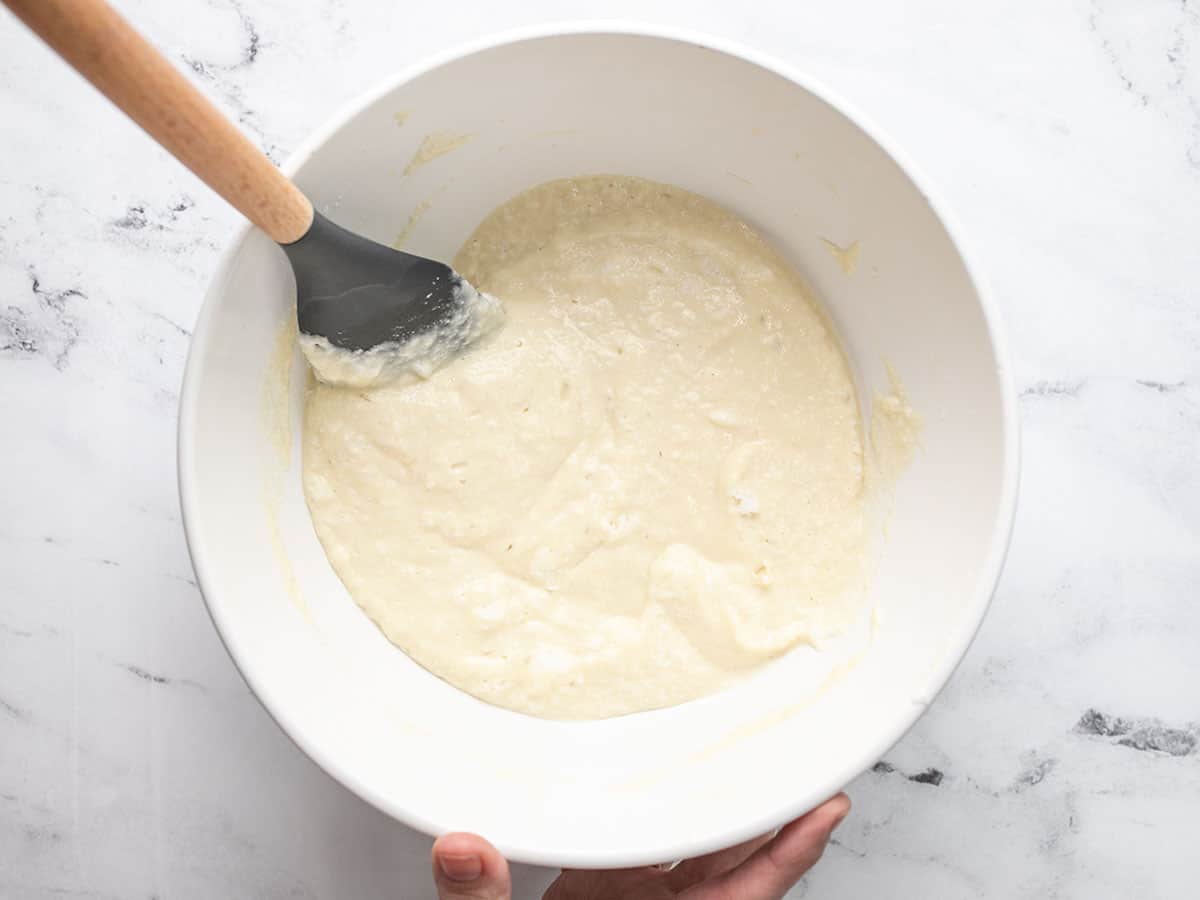 Overhead shot of pancake batter in a white bowl with a wood handled rubber spatula in it.