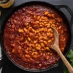 Overhead view of baked beans in the skillet with a wooden spoon.