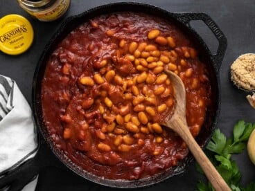 Overhead view of baked beans in the skillet with a wooden spoon.