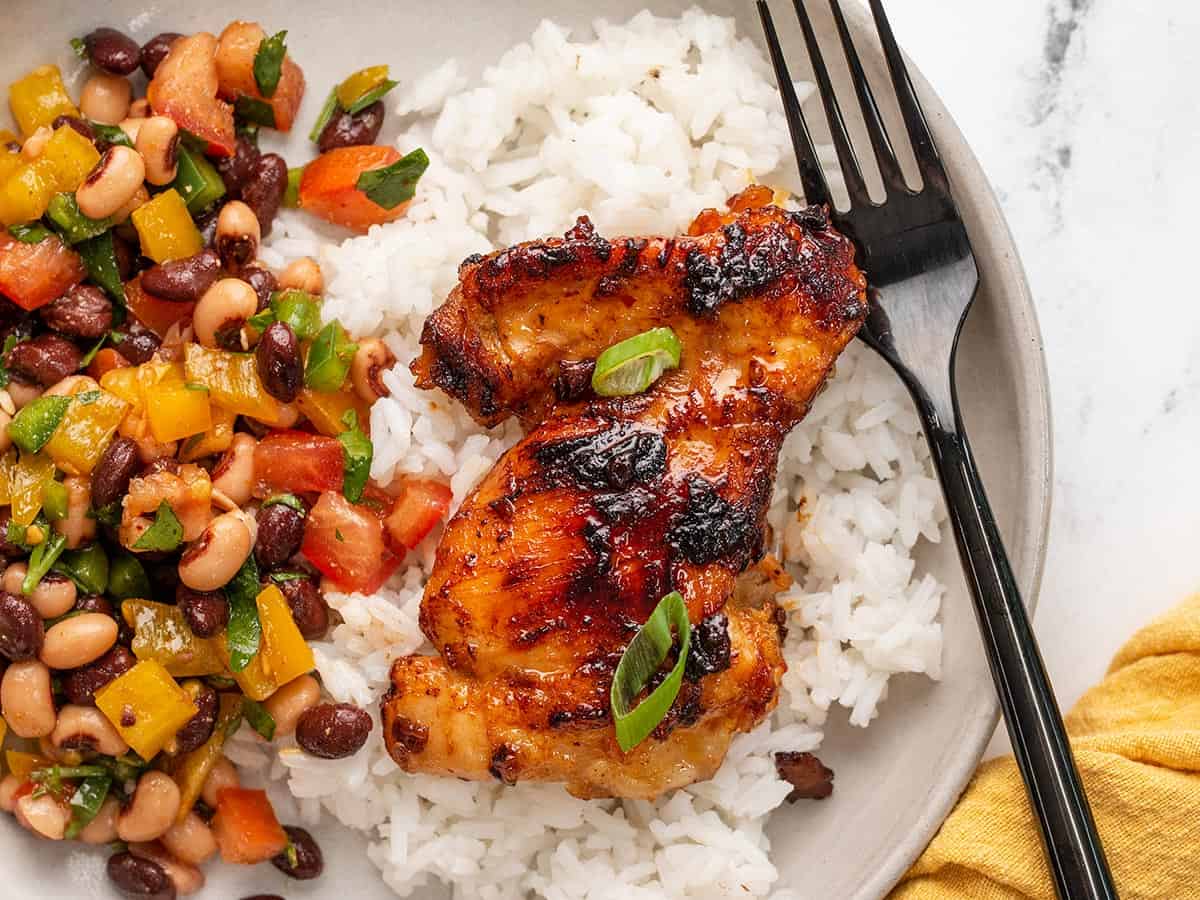 A piece of honey chipotle chicken on a bed of rice with bean salad on the side.