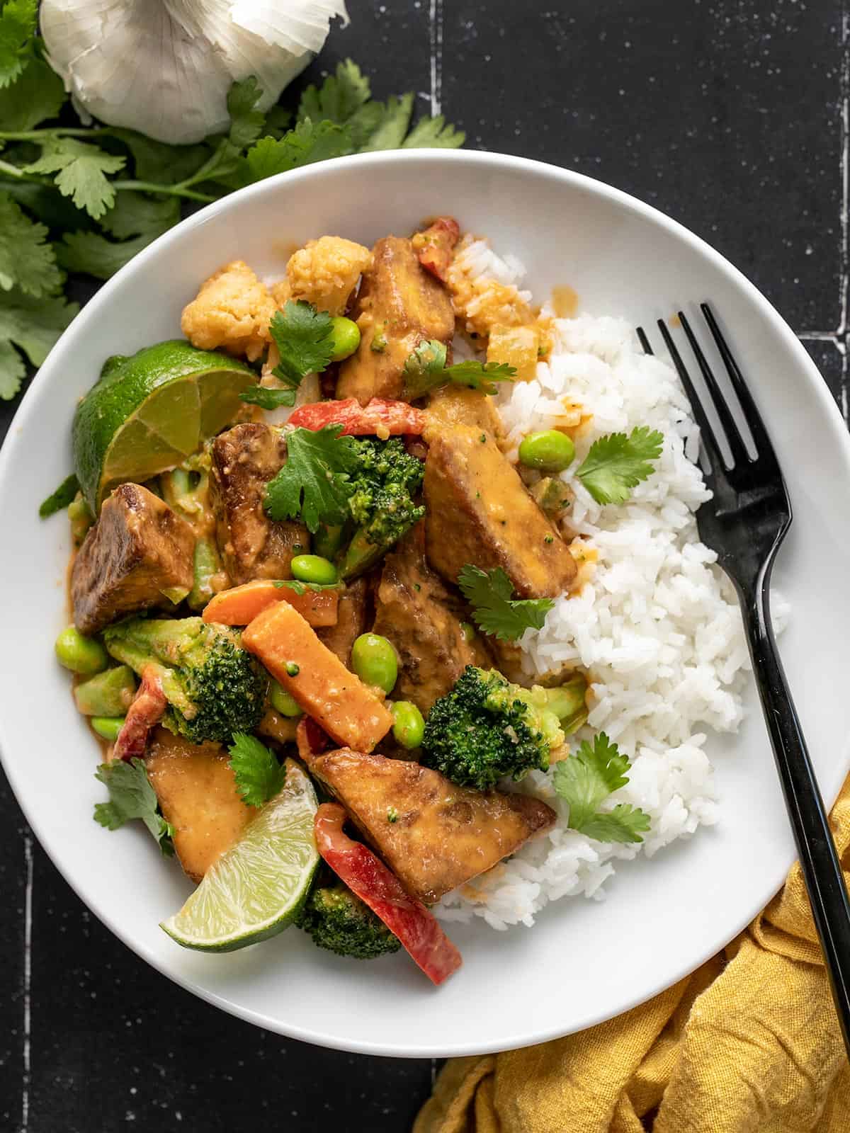 A bowl of peanut tofu with rice, lime wedges, and cilantro.
