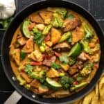 Overhead view of a skillet full of peanut tofu with limes and cilantro.