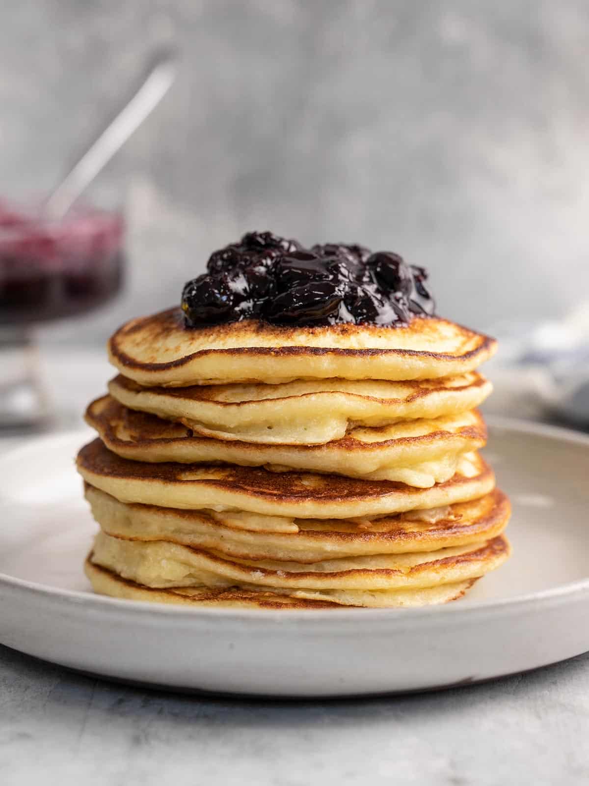 Side shot of a stack of ricotta pancakes with blueberry sauce on top.