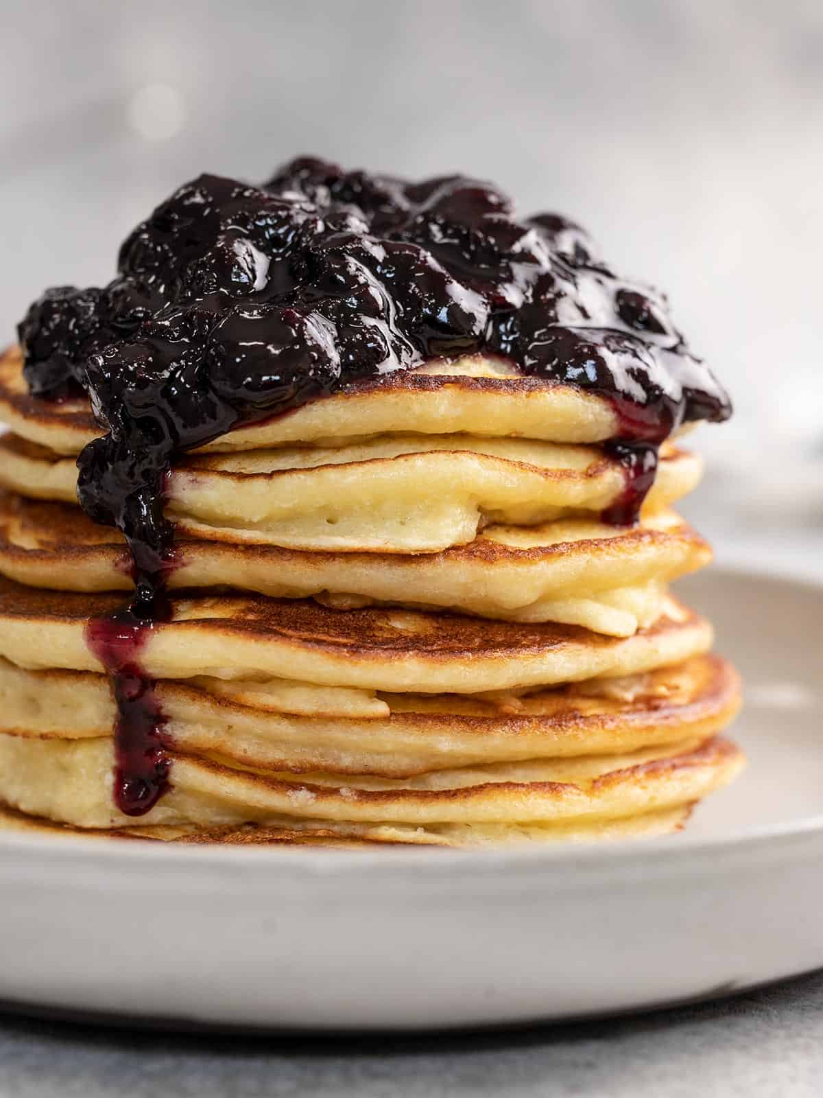 Side shot of a stack of ricotta pancakes with blueberry sauce on top.