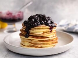 Side shot of a stack of ricotta pancakes with blueberry sauce on top.