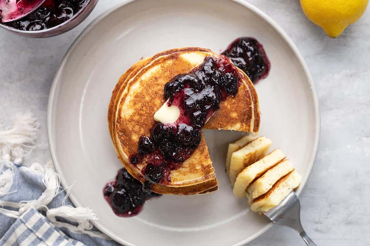 Overhead shot of ricotta pancake stack with blueberry sauce and a fork with a slice of the stack on it.