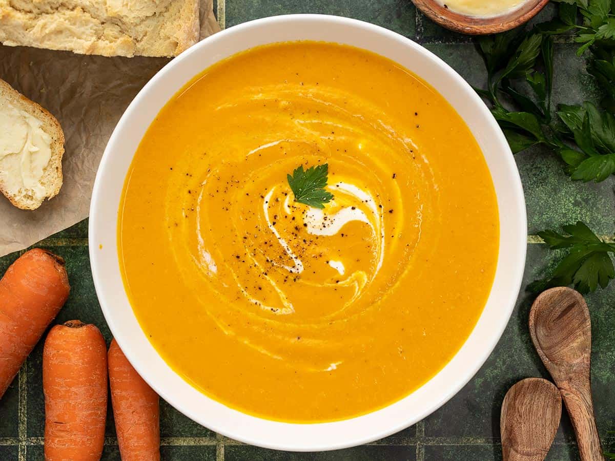 Overhead shot of carrot soup in a white bowl with sour cream swirled in it.