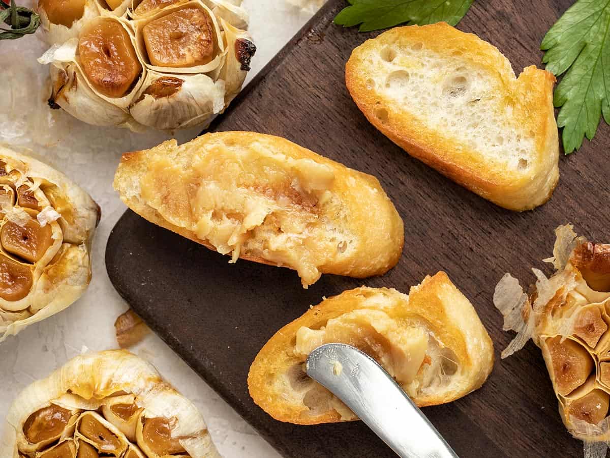 Roasted garlic being spread on a toasted piece of bread.