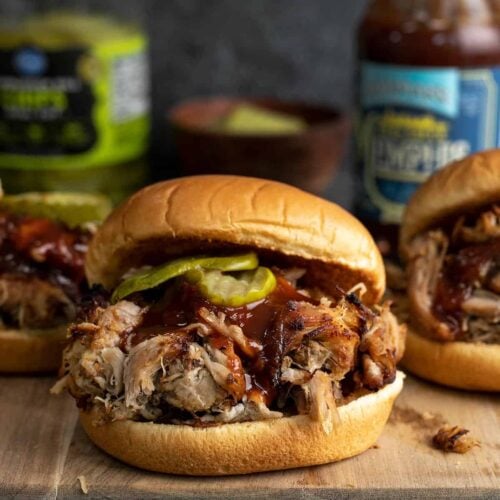 Three slow cooker pulled pork sandwiches on a wooden cutting board.