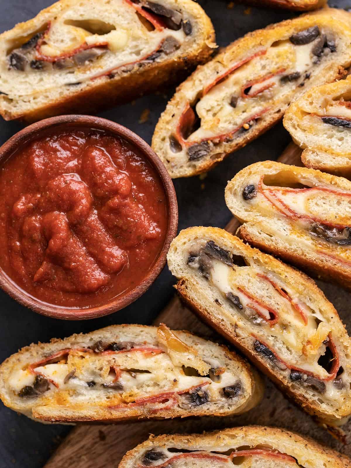Overhead view of slices of stromboli next to a bowl of pizza sauce.