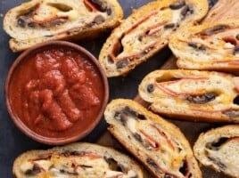 Overhead view of slices of stromboli around a bowl of pizza sauce.