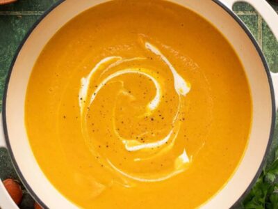 Overhead shot of carrot soup in a white Dutch oven with sour cream swirled in it.