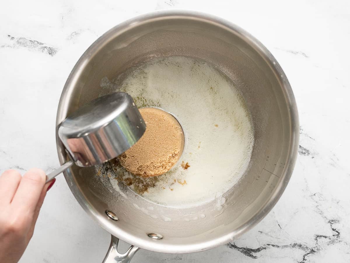 Browns sugar being put in a pot with melted, frothy butter.