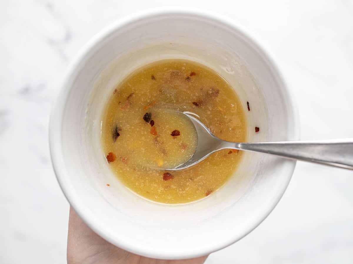 Overhead shot of a spoon mixing hot honey butter in a small white bowl.