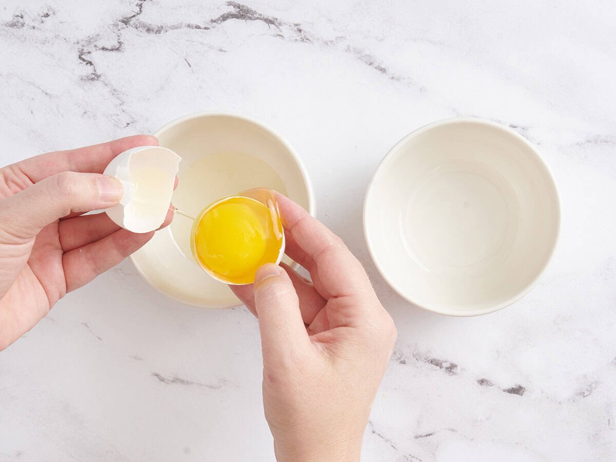 Hands separating egg whites from an egg yolk.