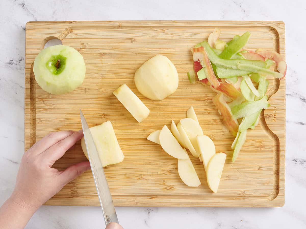 Hands using a knife to peel and slice apples.
