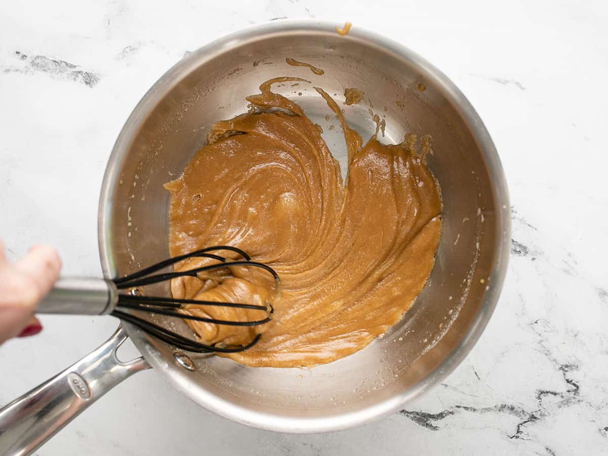 Whisk stirring caramel sauce in a pot.