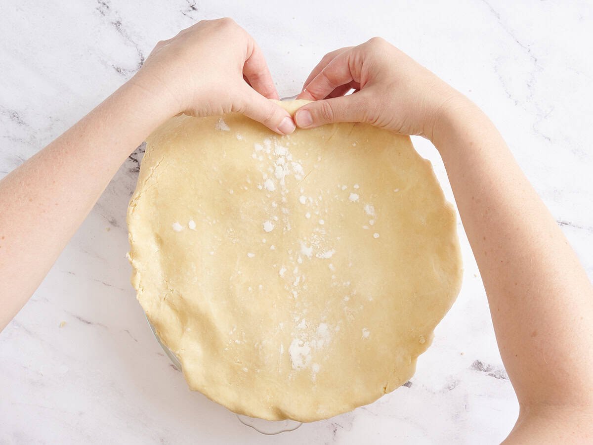 Hands crimpling the edges of an apple pie.