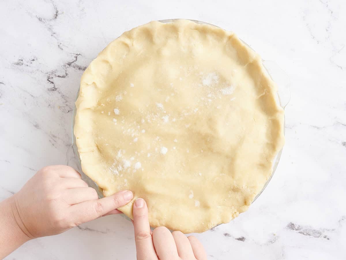 Fingers crimping the edges of the top crust for a homemade apple pie.