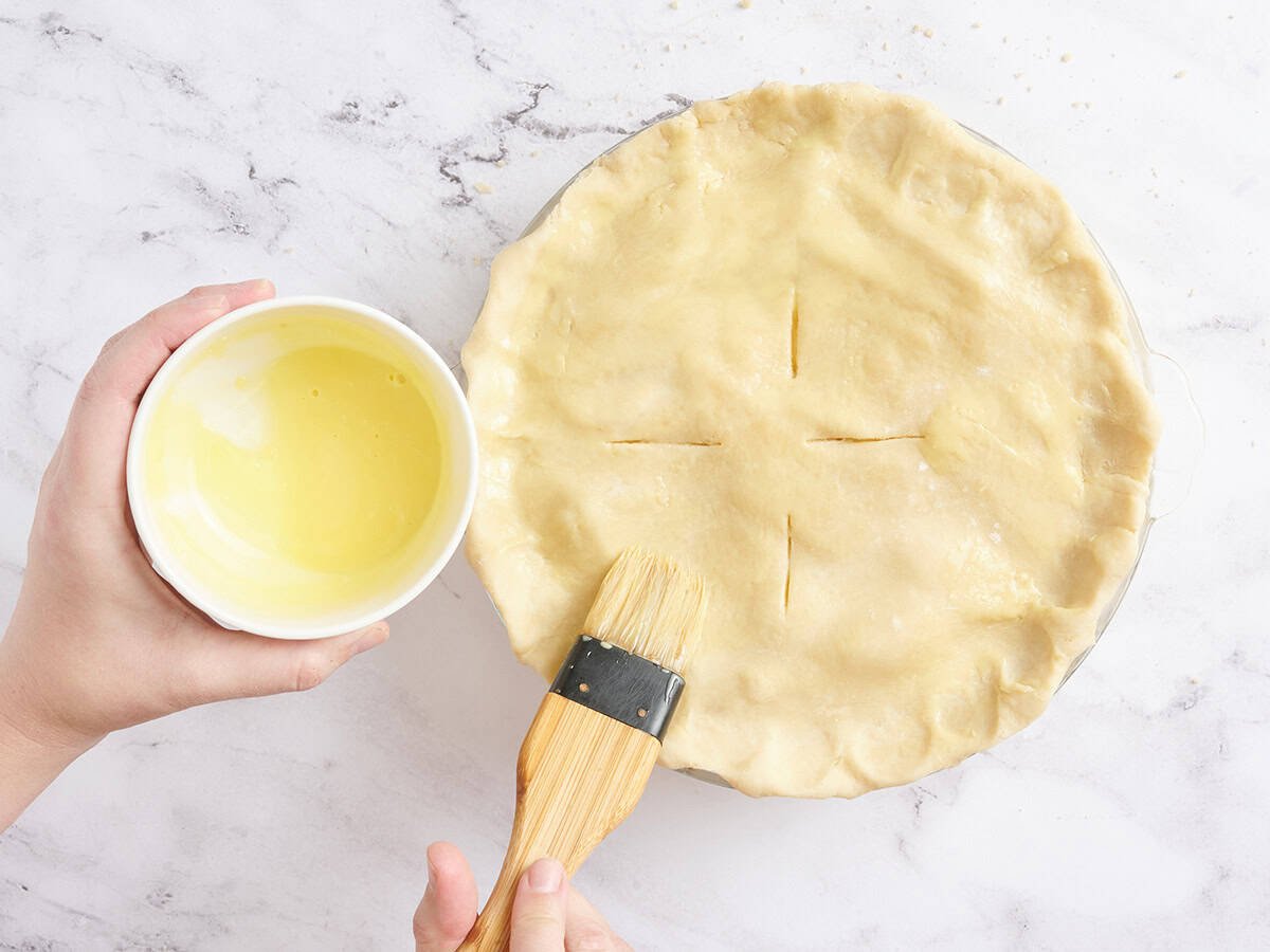An unbaked apple pie being brushed with egg wash.