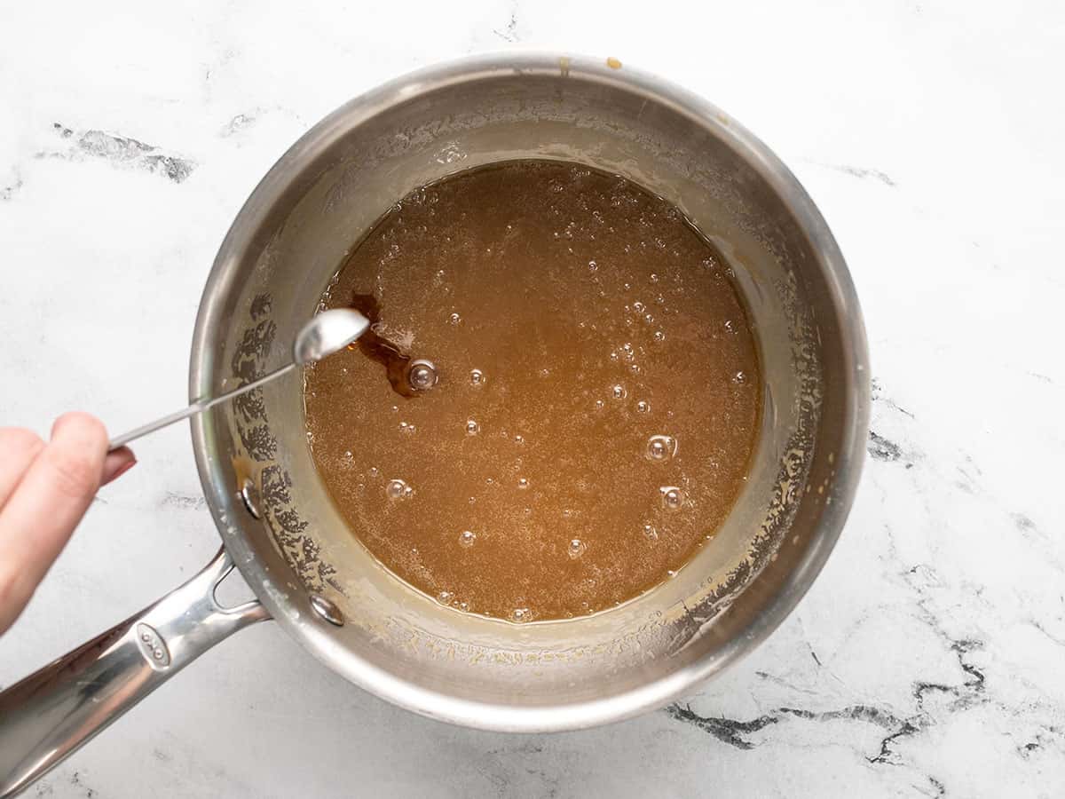 Vanilla being put in caramel sauce in a pot.