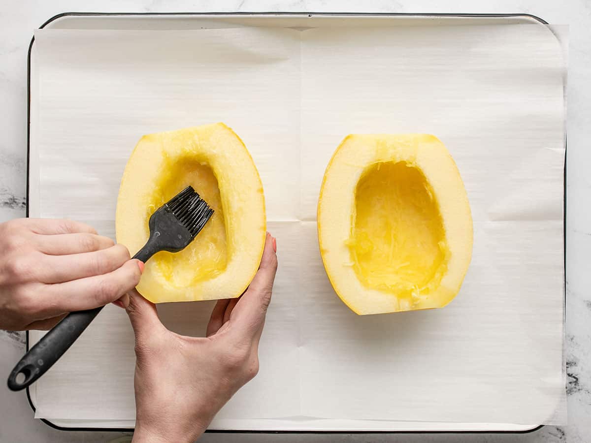 Overhead shot of hands holding a cut squash half and brushing oil on it.