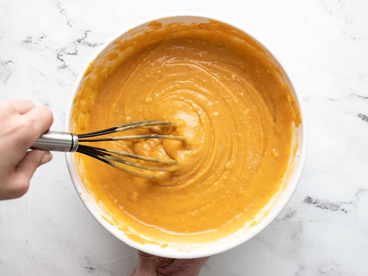 Overhead shot of whisk mixing pumpkin bread batter in a white bowl.