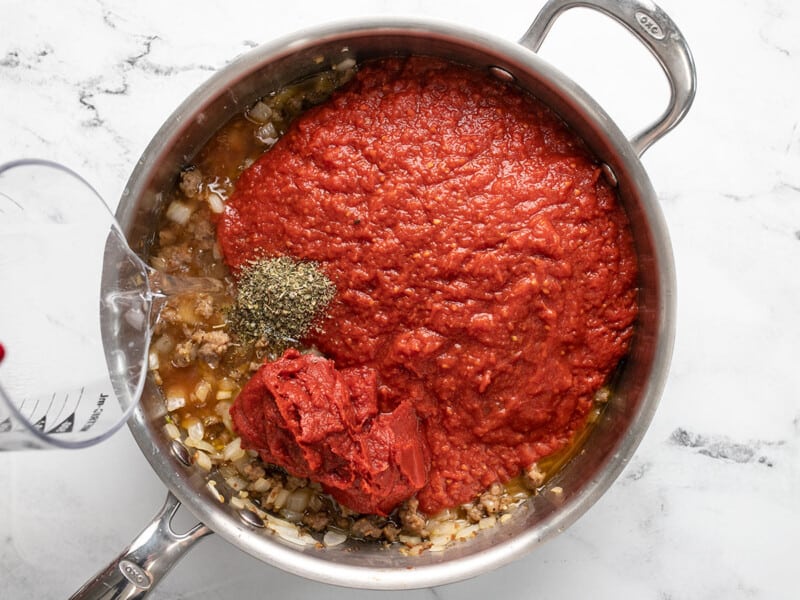 Crushed tomatoes, tomato paste, herbs, and water added to the skillet.