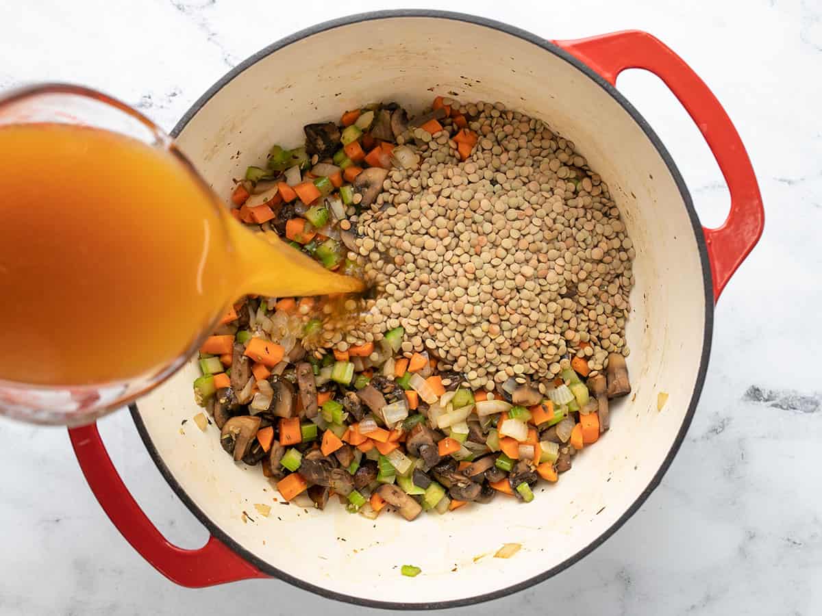 Lentils in the pot and vegetable broth being poured in.