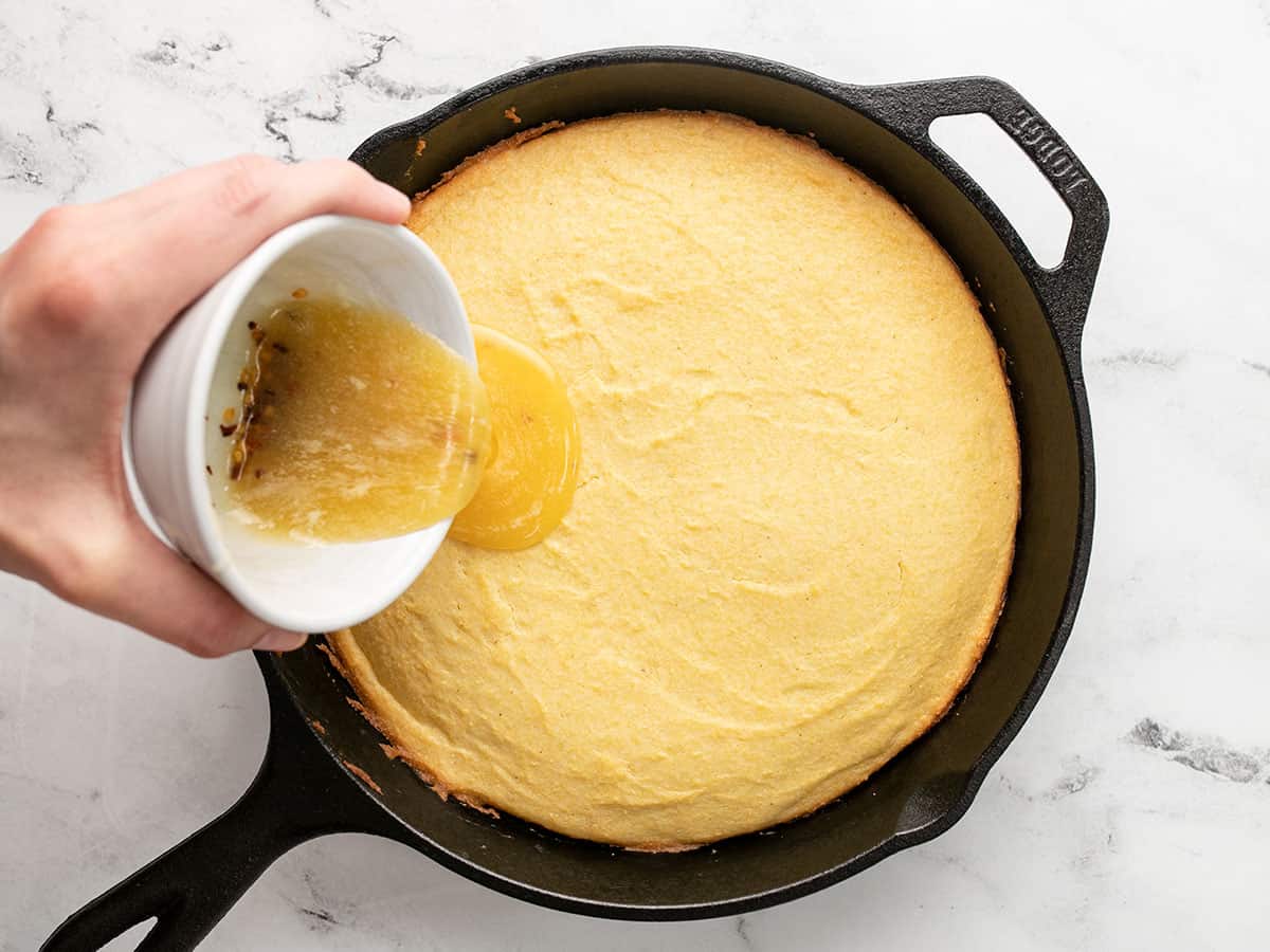 Overhead shot of hot honey butter being drizzled onto baked cornbread in a cast iron skillet.