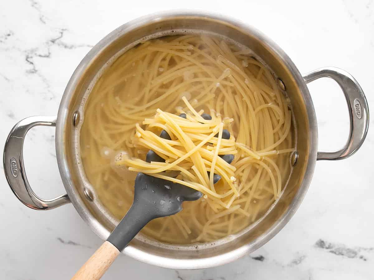 Boiled spaghetti in a pot with a pasta spoon.