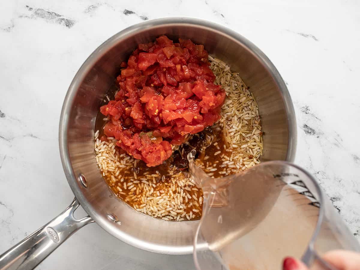 Spanish rice mix and Rotel in a pot, water being poured in the side. 