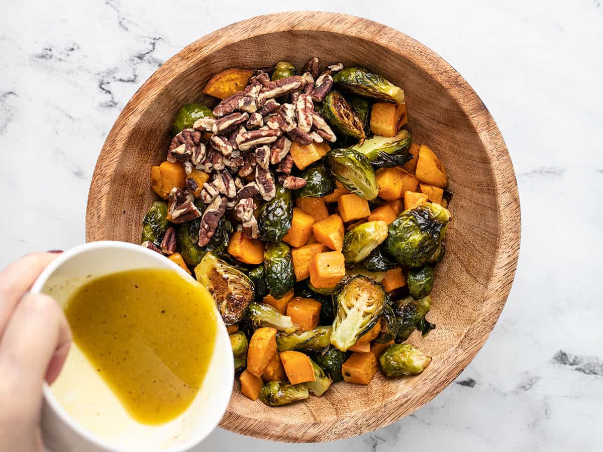 Dressing being poured over the bowl of vegetables with pecans.