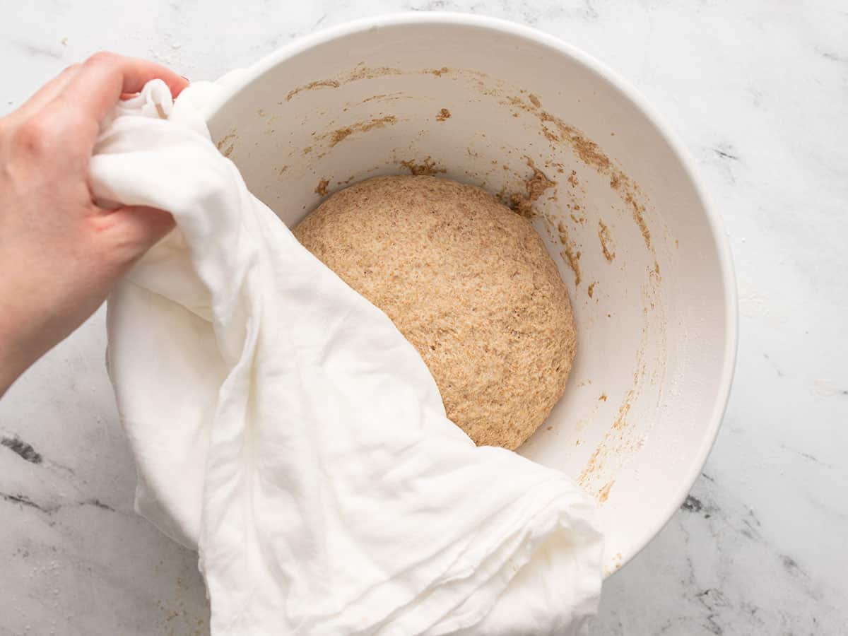 Kneaded dough in the mixing bowl half covered with a cloth.