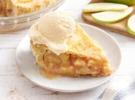 Side view of a slice of apple pie topped with a scoop of vanilla ice cream.