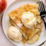 Overhead shot of a slice of apple pie on a white plate with two scoops of vanilla ice cream and drizzled with caramel sauce.