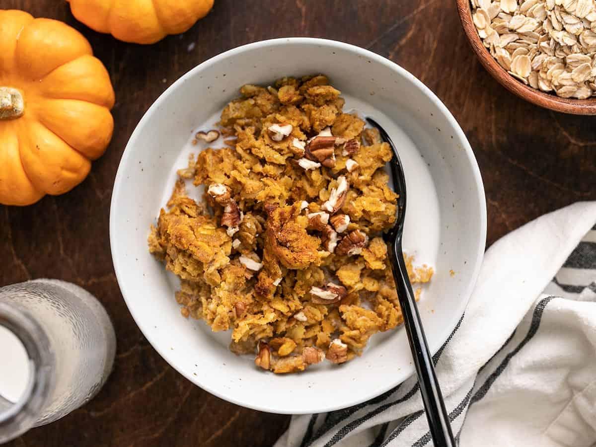 Baked pumpkin pie oatmeal in a bowl with nuts and milk.