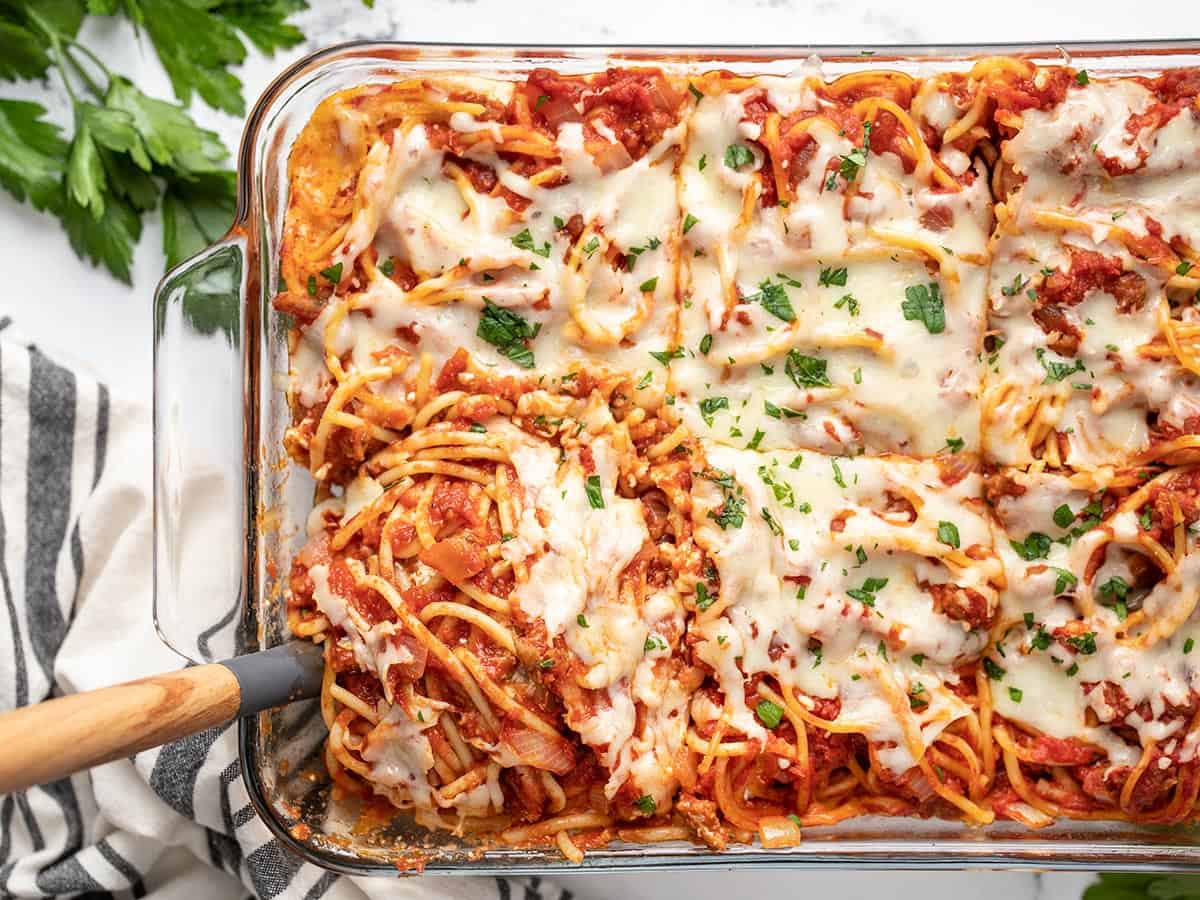 Overhead view of baked spaghetti being scooped out of the casserole dish.