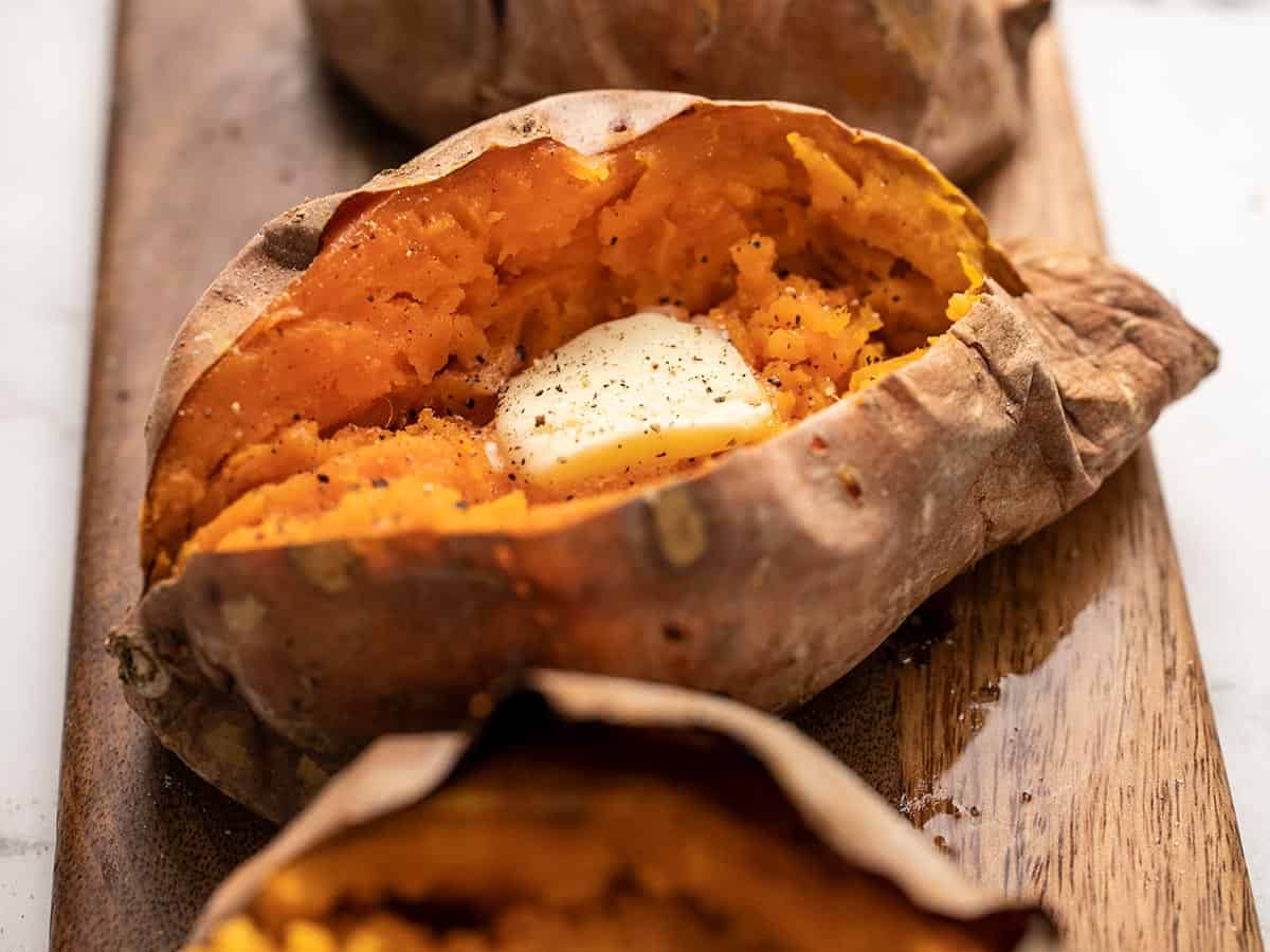 Side view of baked sweet potatoes on a wooden cutting board. 