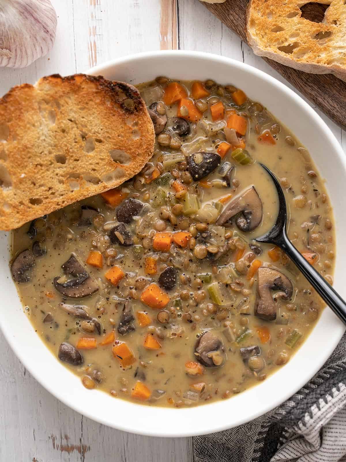 Close up overhead view of a bowl of creamy lentil vegetable soup with bread on the side.