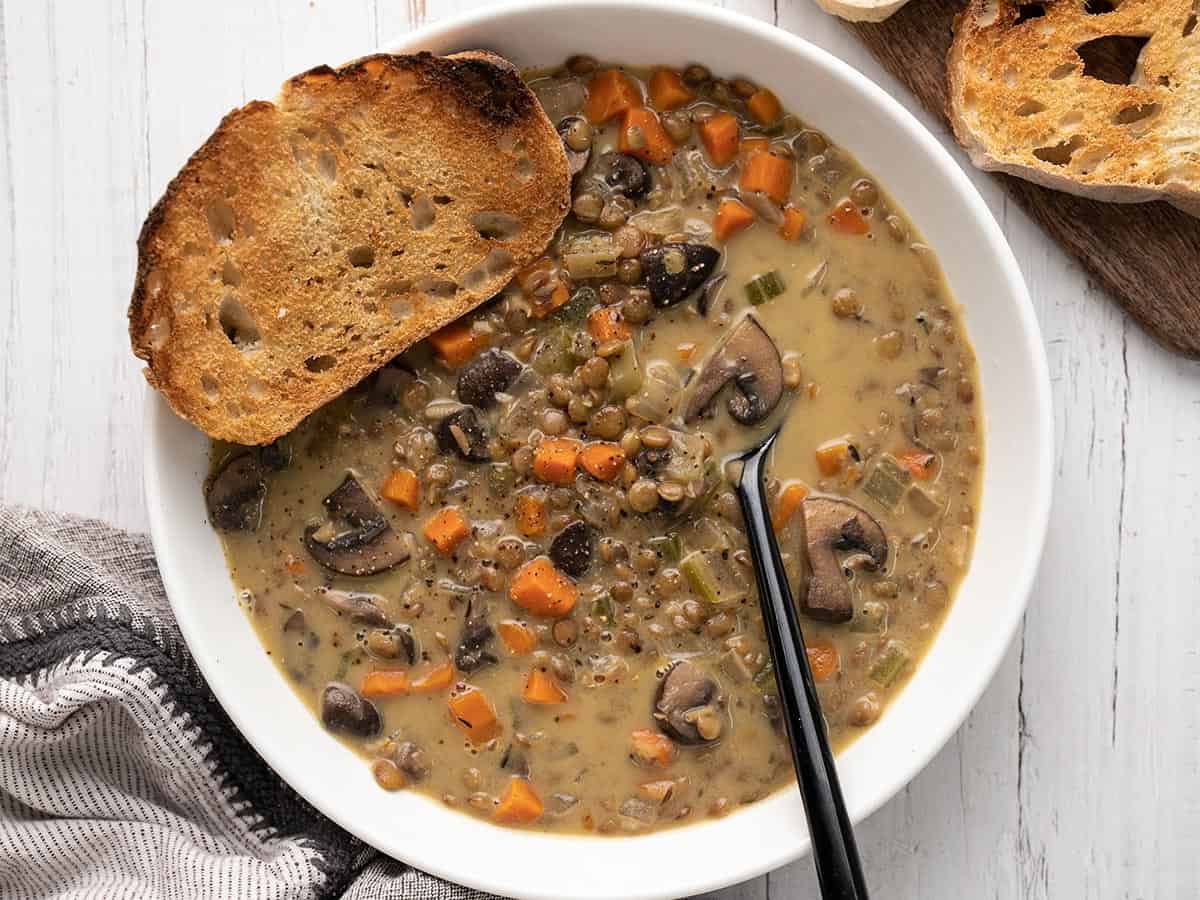 Overhead view of a bowl of creamy lentil vegetable soup with a piece of bread.