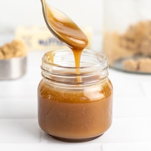 Side shot of a spoon drizzling caramel sauce in a mason jar.