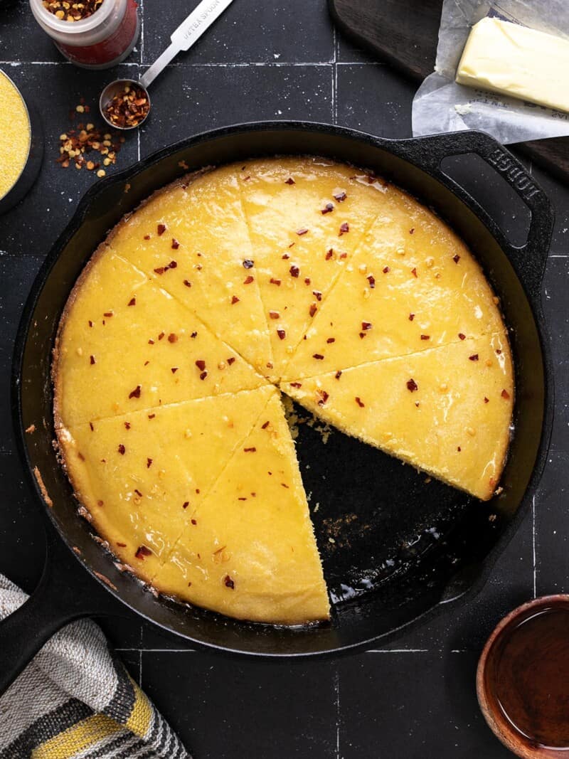 Overhead shot of cornbread in a cast iron skillet with a wedge taken out.