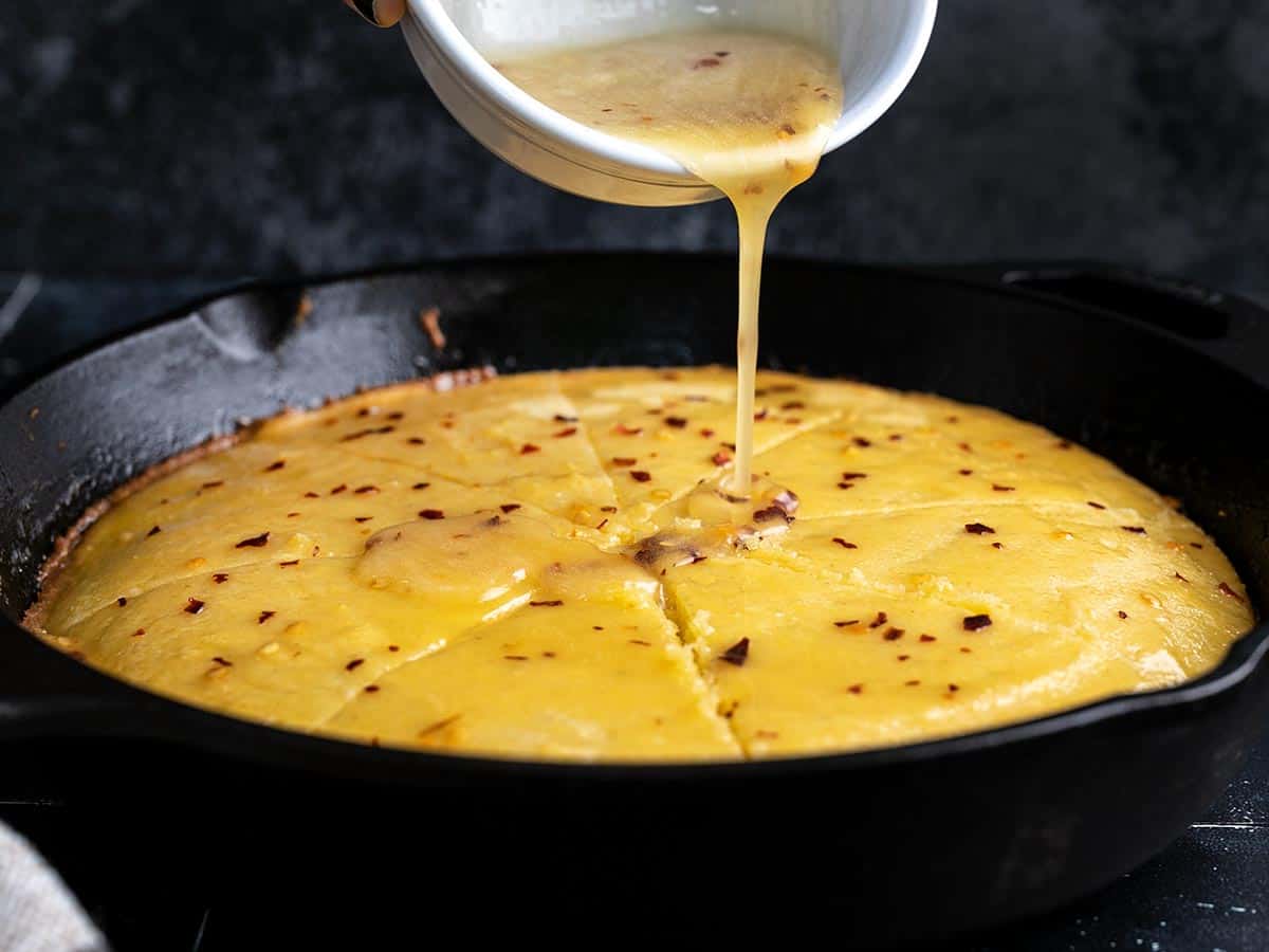 Side shot of hot honey butter being drizzled on cornbread.