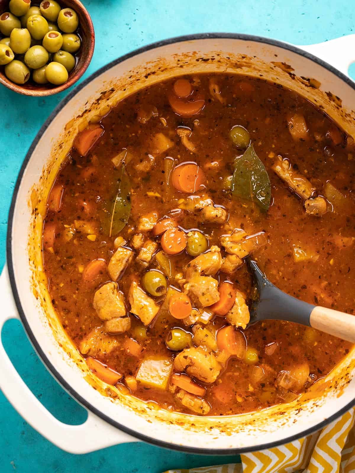 Overhead shot of Guisado de Pollo in a white Dutch oven with a spoon in it.