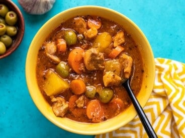 Overhead shot of Guisado de Pollo in a yellow bowl with a spoon in it.