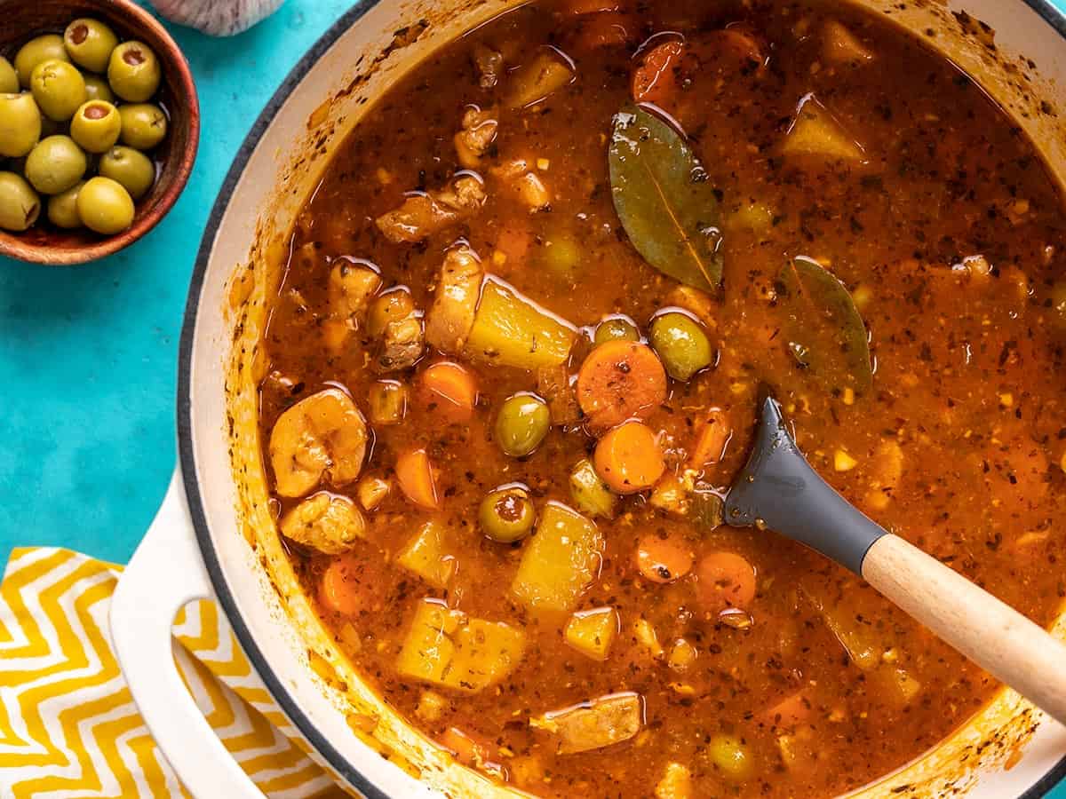 Overhead shot of Guisado de Pollo in a white Dutch oven with a spoon in it.