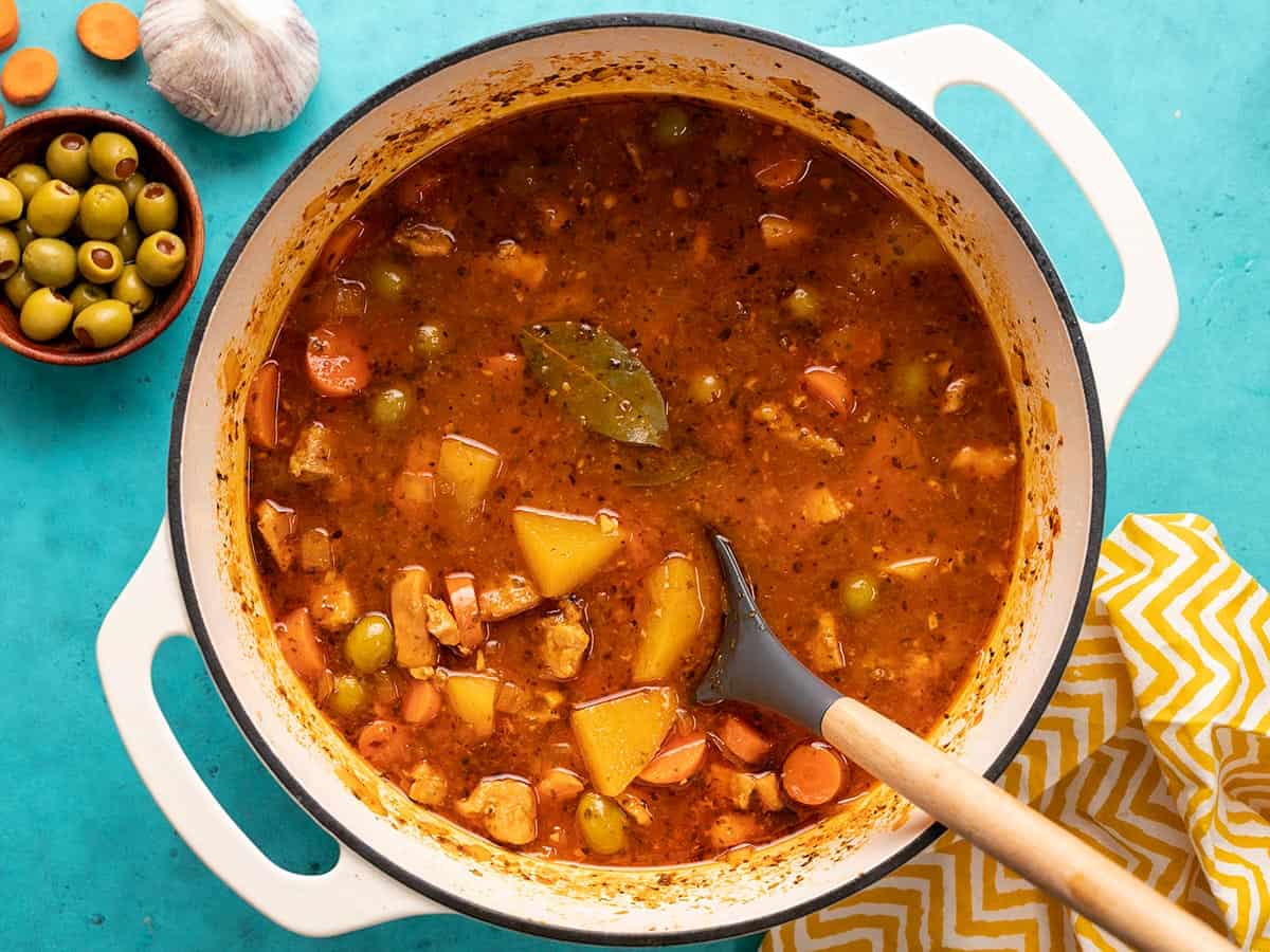 Overhead shot of Guisado de Pollo in a white Dutch oven with a spoon in it.